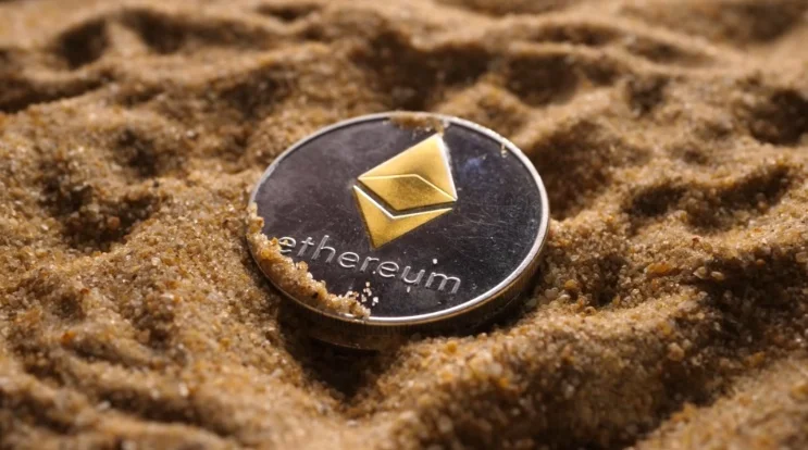 A physical Ethereum coin resting in the sand