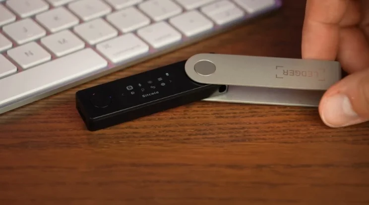 A Ledger hardware wallet sitting on a wooden desk next to a computer keyboard.