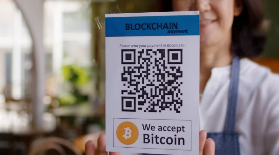 A shopkeeper presenting a sign that says 'We accept Bitcoin' with a QR code